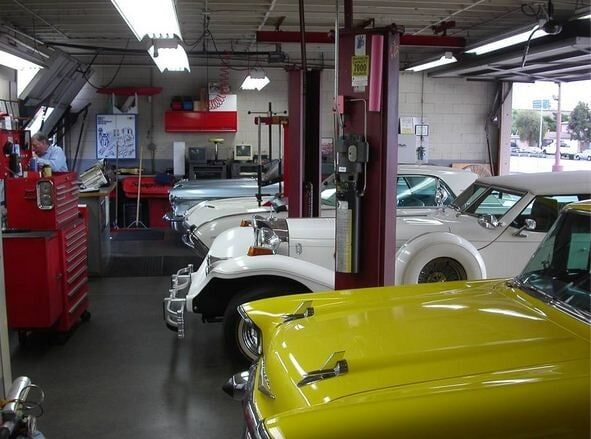 Auto repair shop with classic cars, including a bright yellow car in the foreground and white cars under lifts.