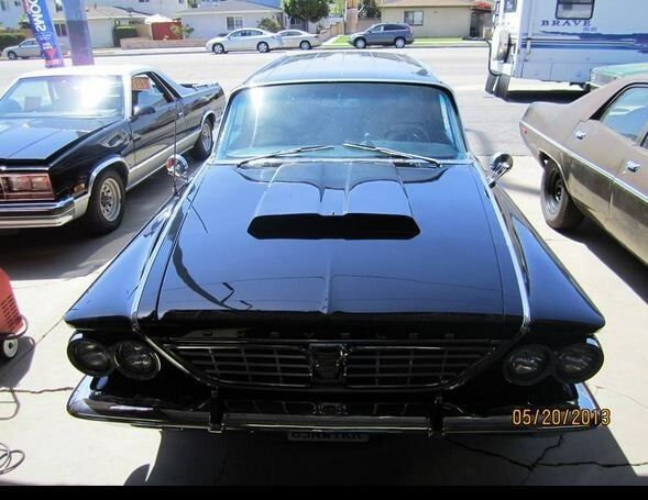 Front view of a black classic car with a hood scoop parked outdoors among other cars.
