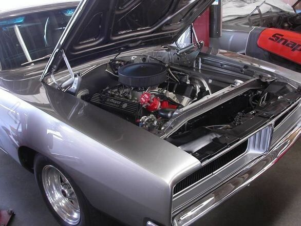 Classic silver muscle car with open hood, showing a modified engine at a car show
