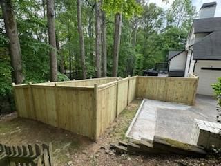 Wooden fence surrounding a patio area next to a house and trees.