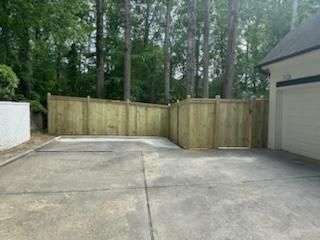 Concrete driveway with wooden fence and trees in the background. Garage on the right.