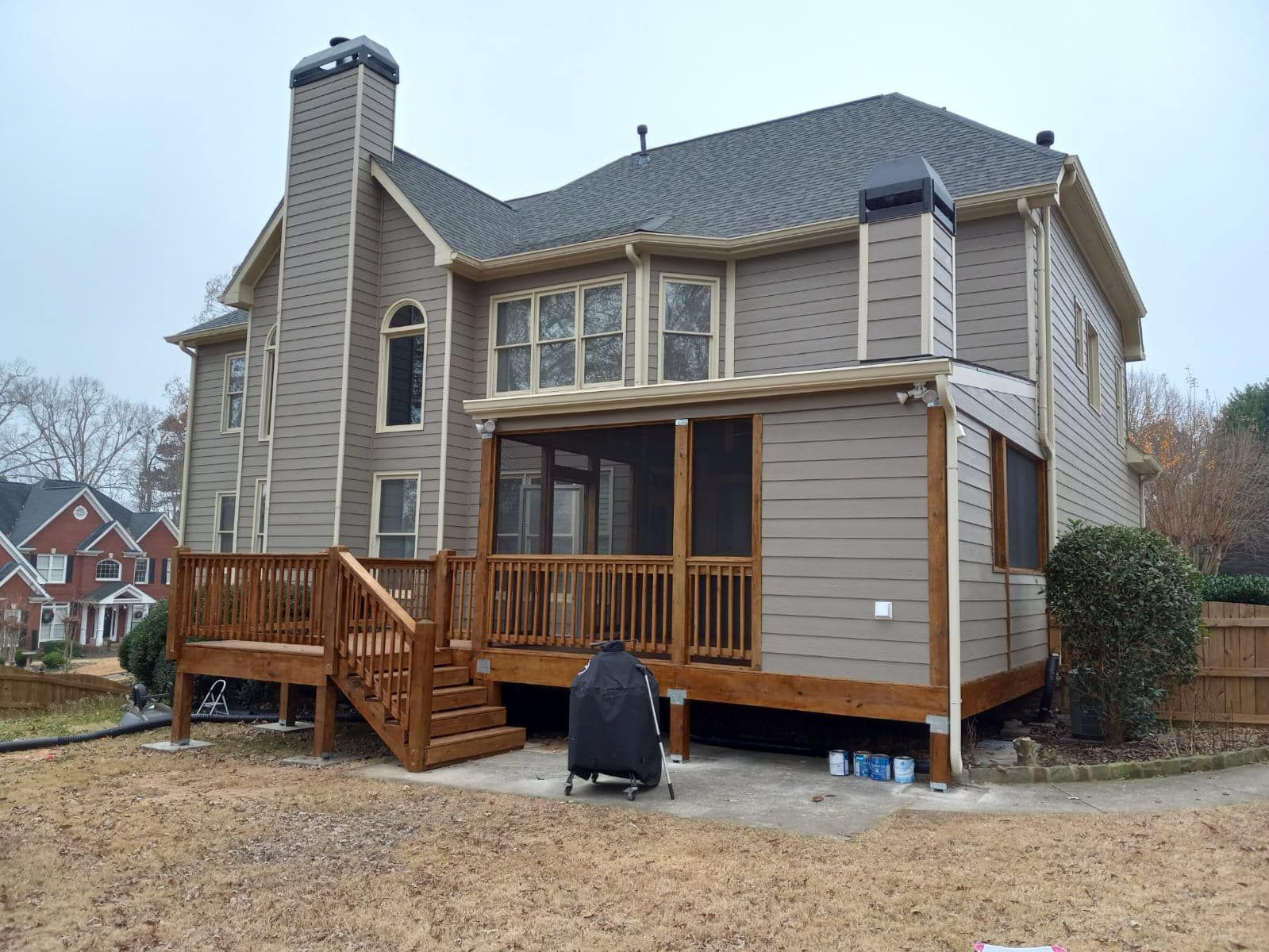 Back of a house with a wooden deck, screened-in porch, and tan siding on a cloudy day.