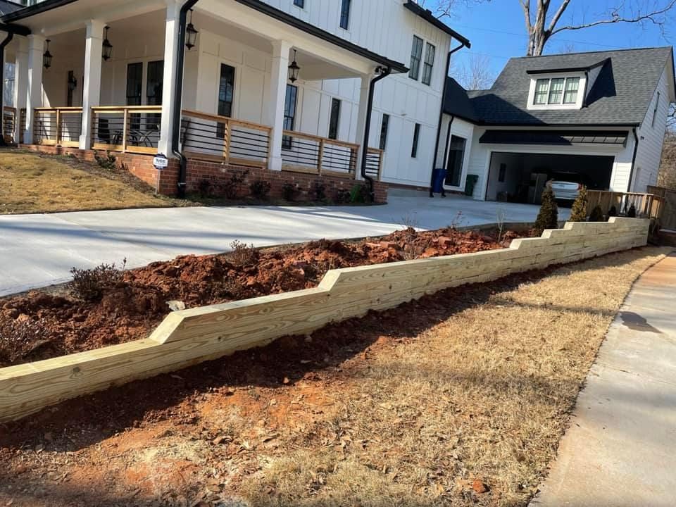 A wooden retaining wall with dirt and a house in the background.