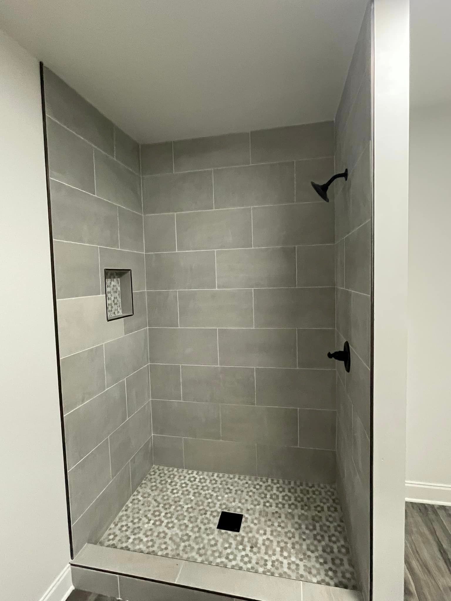 Gray tiled shower with patterned floor and black fixtures.
