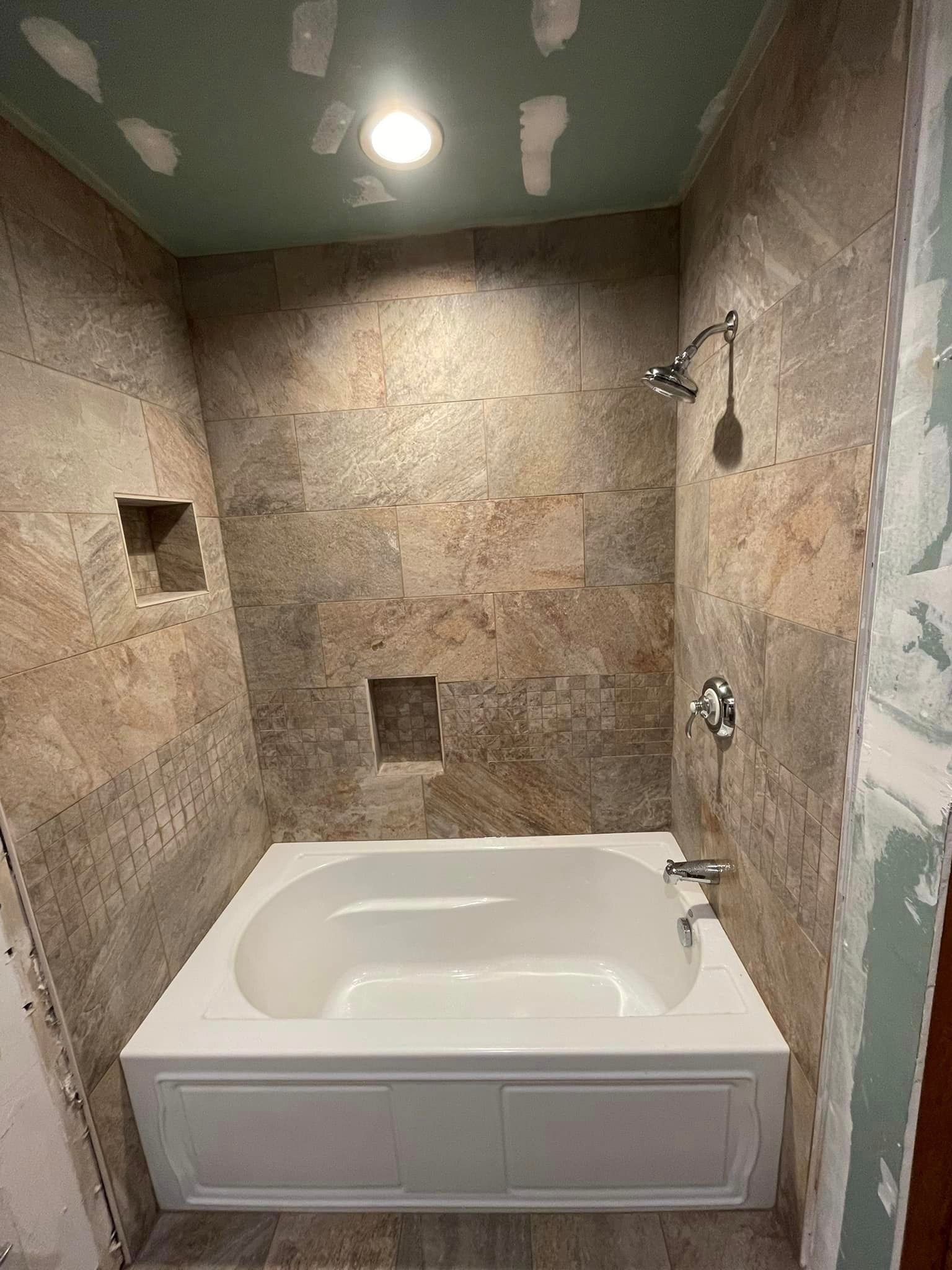 Bathroom with a white bathtub and brown tiled walls, showerhead and niche.