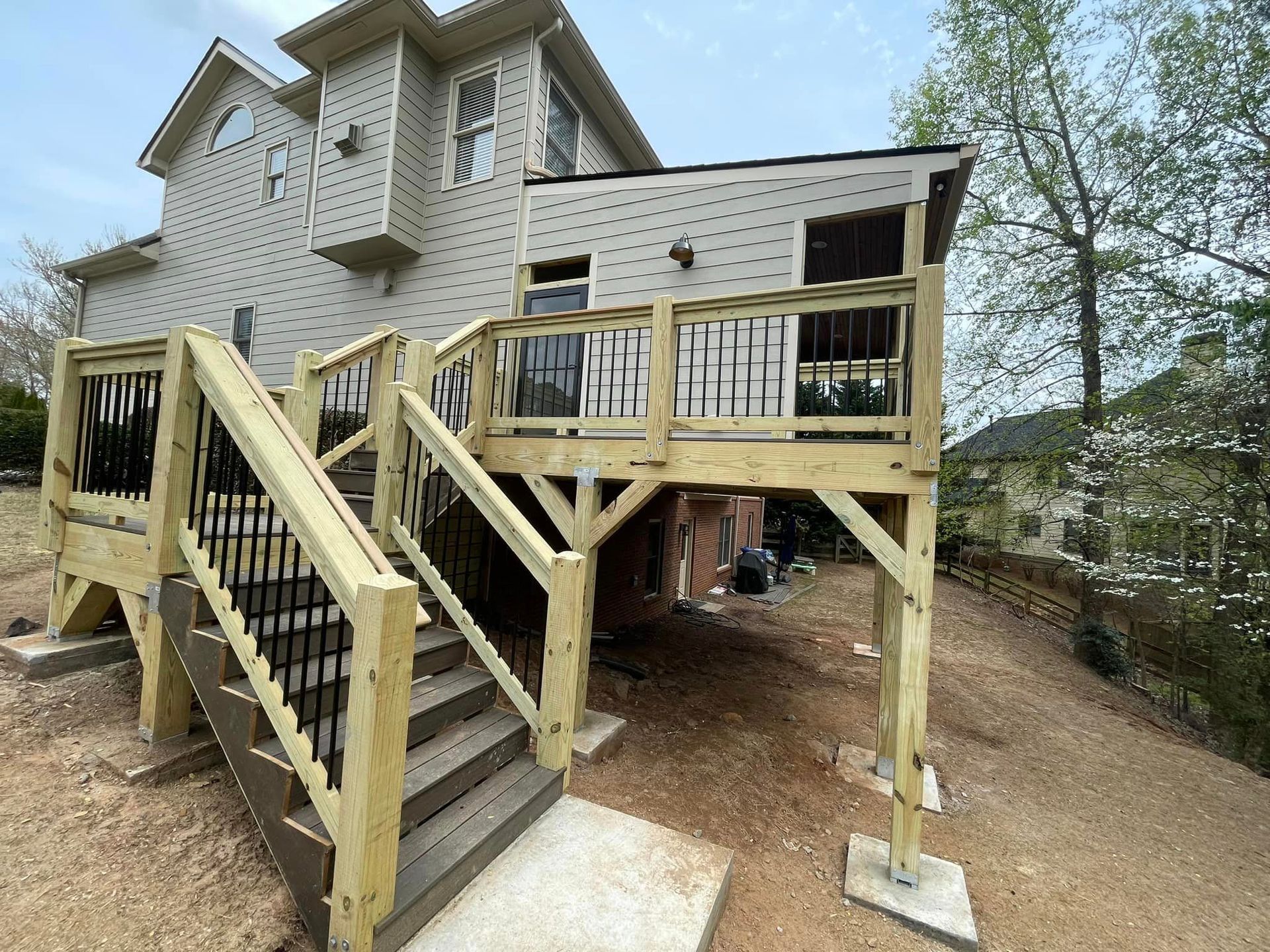 New wooden deck with stairs attached to a two-story beige house on a sloped yard.