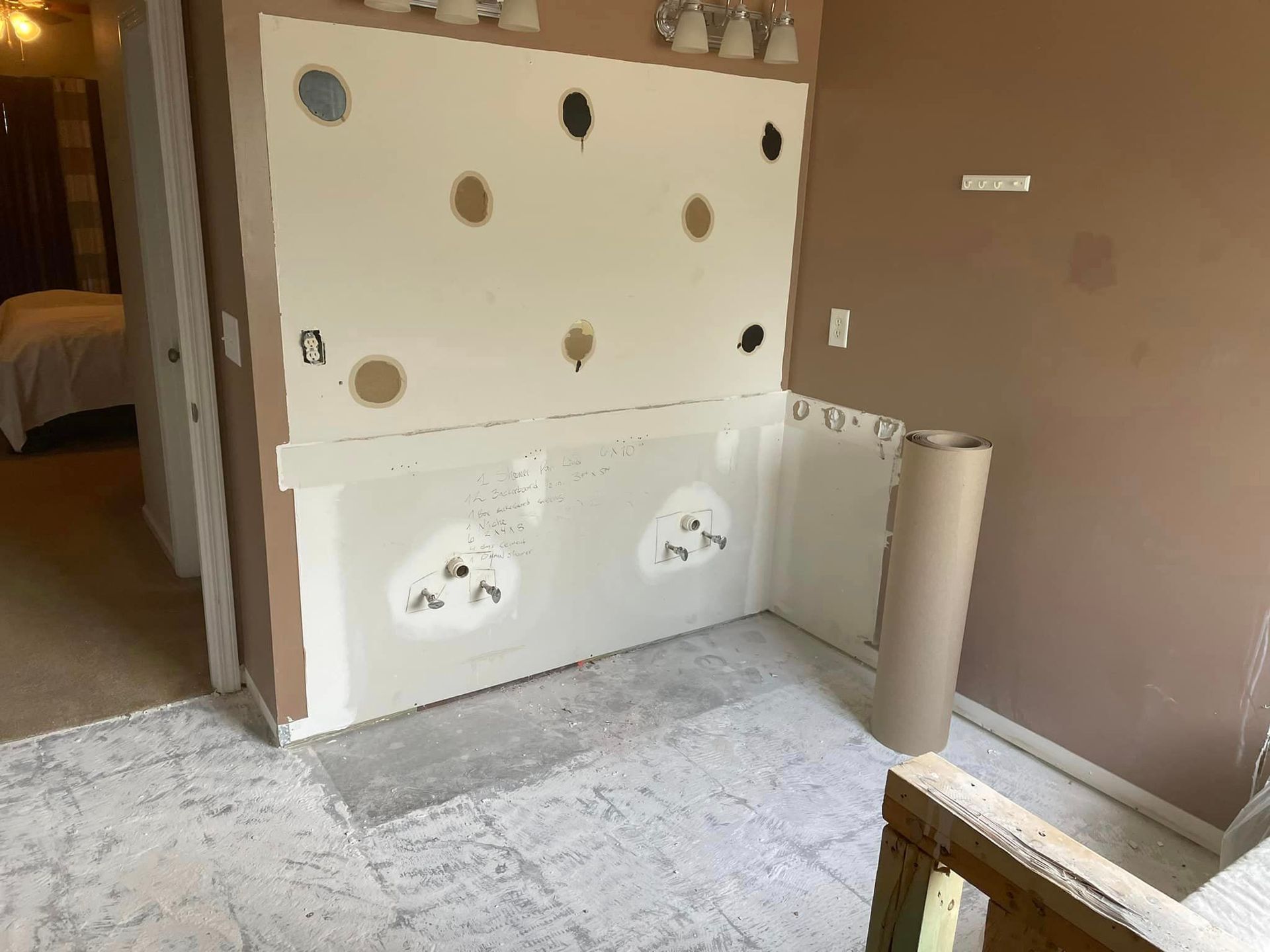 Room under construction, drywall on walls, flooring partially covered, roll of paper beside wall.