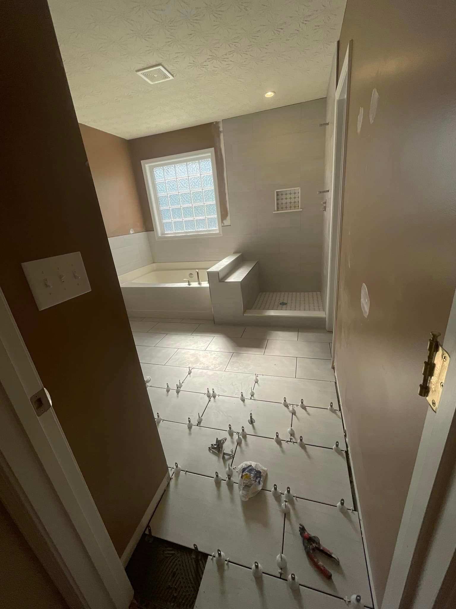 Bathroom renovation: beige tiled floor, white tub and shower, brown walls, unfinished tile work in progress.