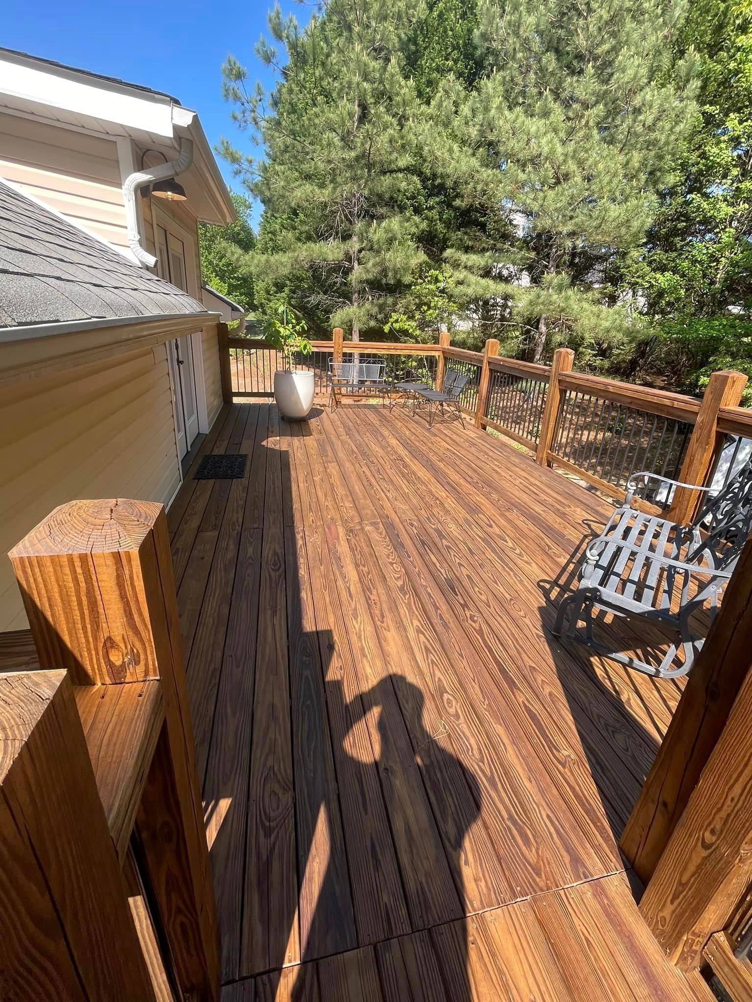 Wooden deck with railing, a white pot, and tall trees in the background. Shadow of a person is visible.