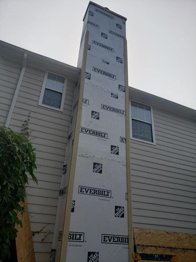 Exterior chimney construction, wrapped in white insulation, against a light-colored house.