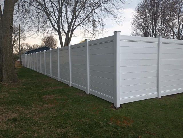 White vinyl privacy fence in a grassy yard, under a cloudy sky.