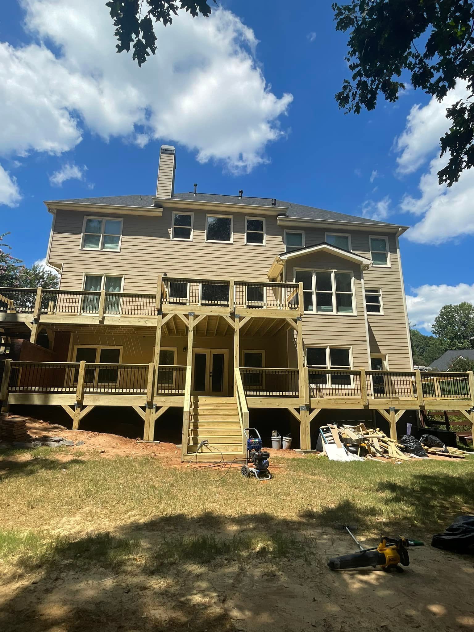 Back of a multi-story house with two wooden decks under a blue sky.