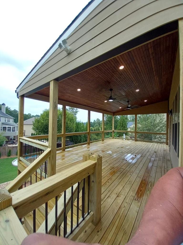 Wooden deck with covered ceiling, ceiling fans, recessed lights, and railing overlooking a yard and trees.