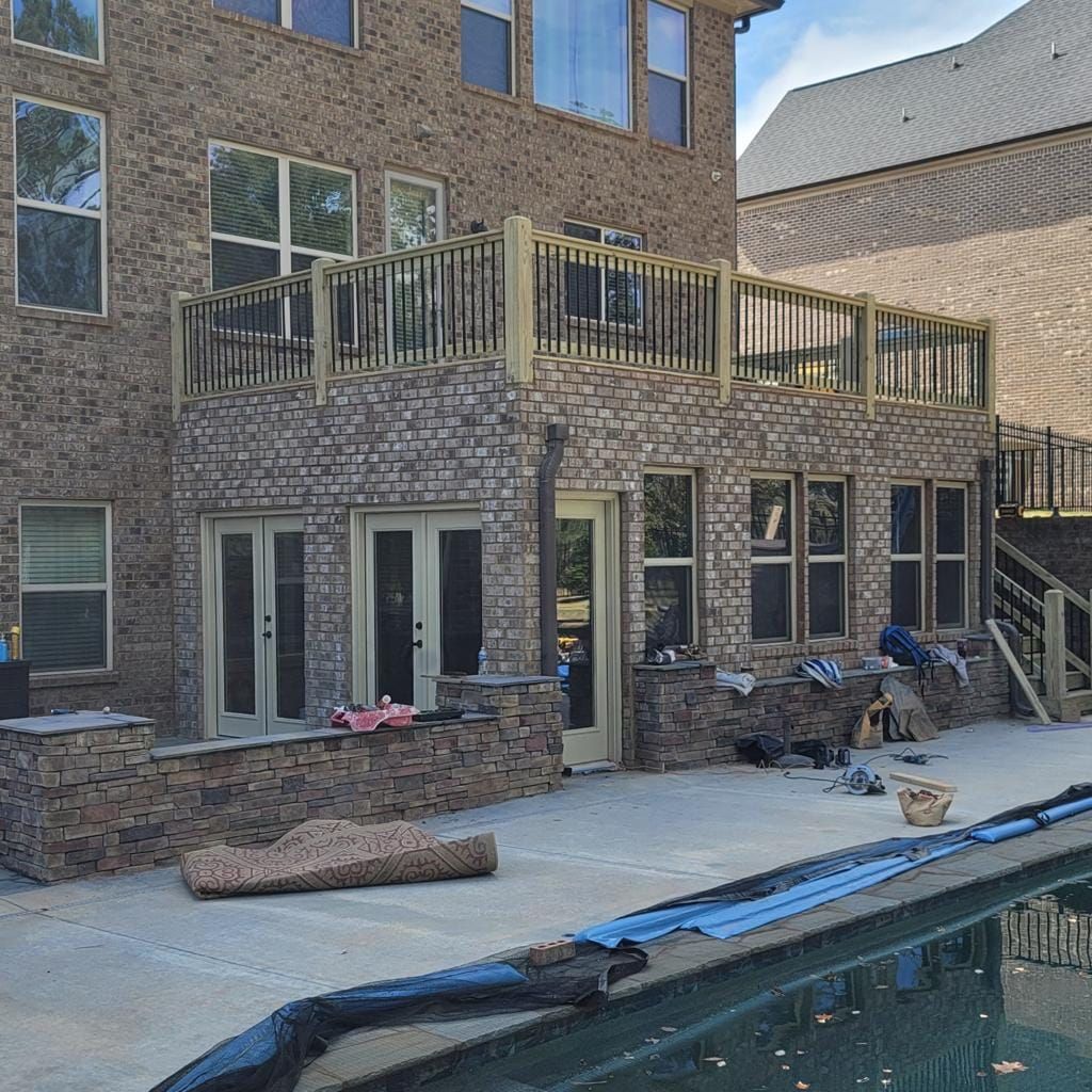 Back of a brick house with a multi-level wooden deck and a pool.