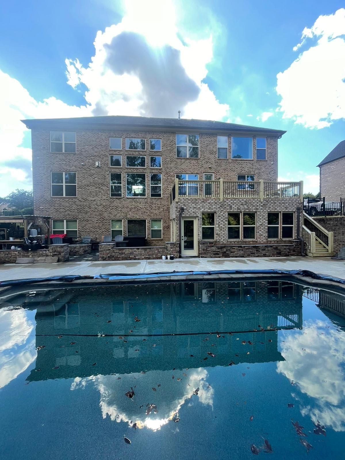 Back of a brick house with a pool in the foreground reflecting clouds in the sky.