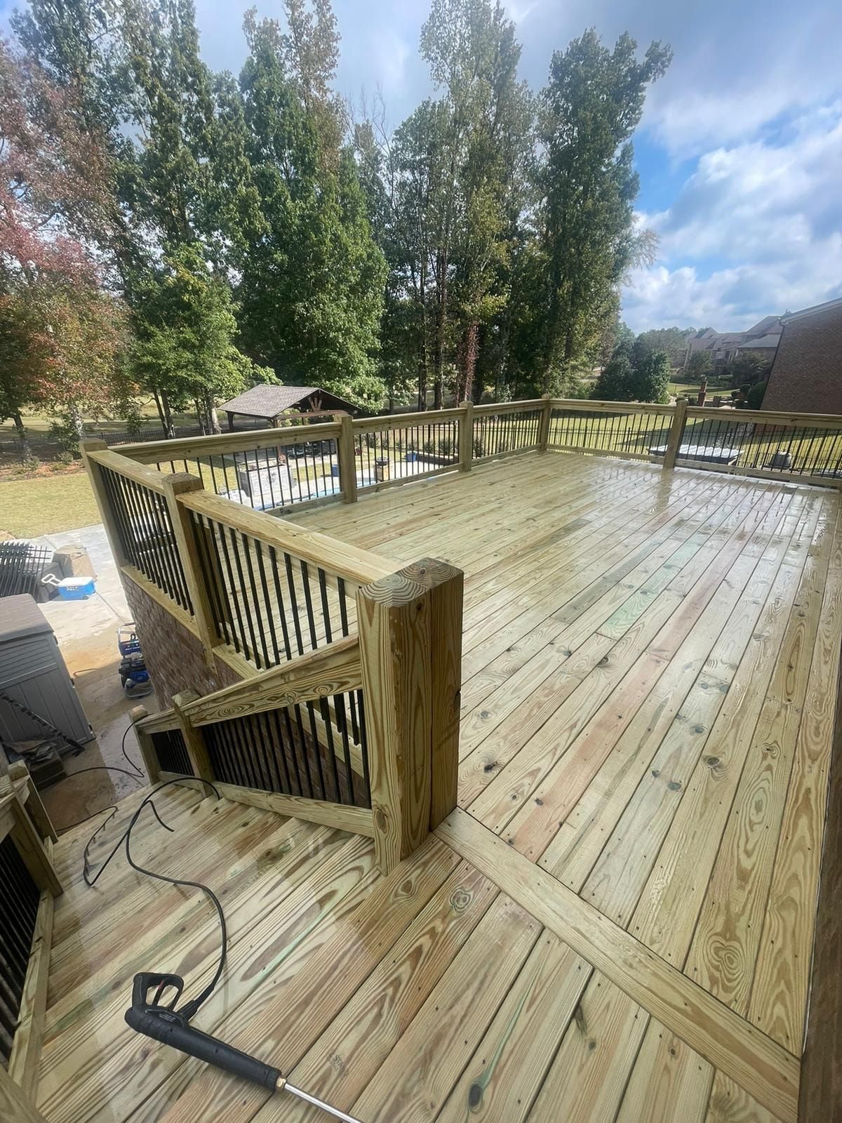 Wooden deck being power washed outdoors with trees in the background.