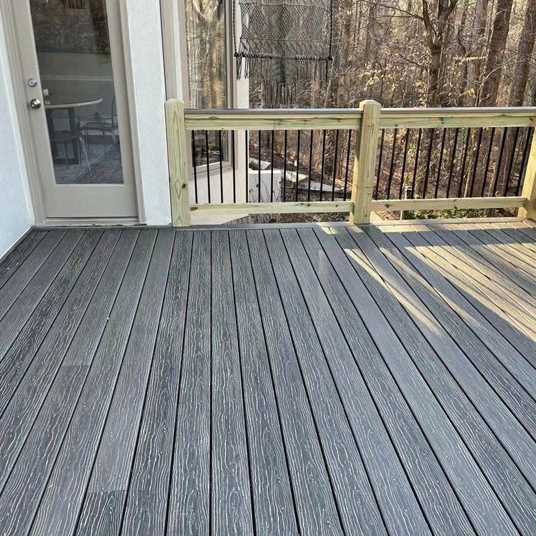 Gray composite deck with a wooden railing and a glass door, overlooking a wooded area.