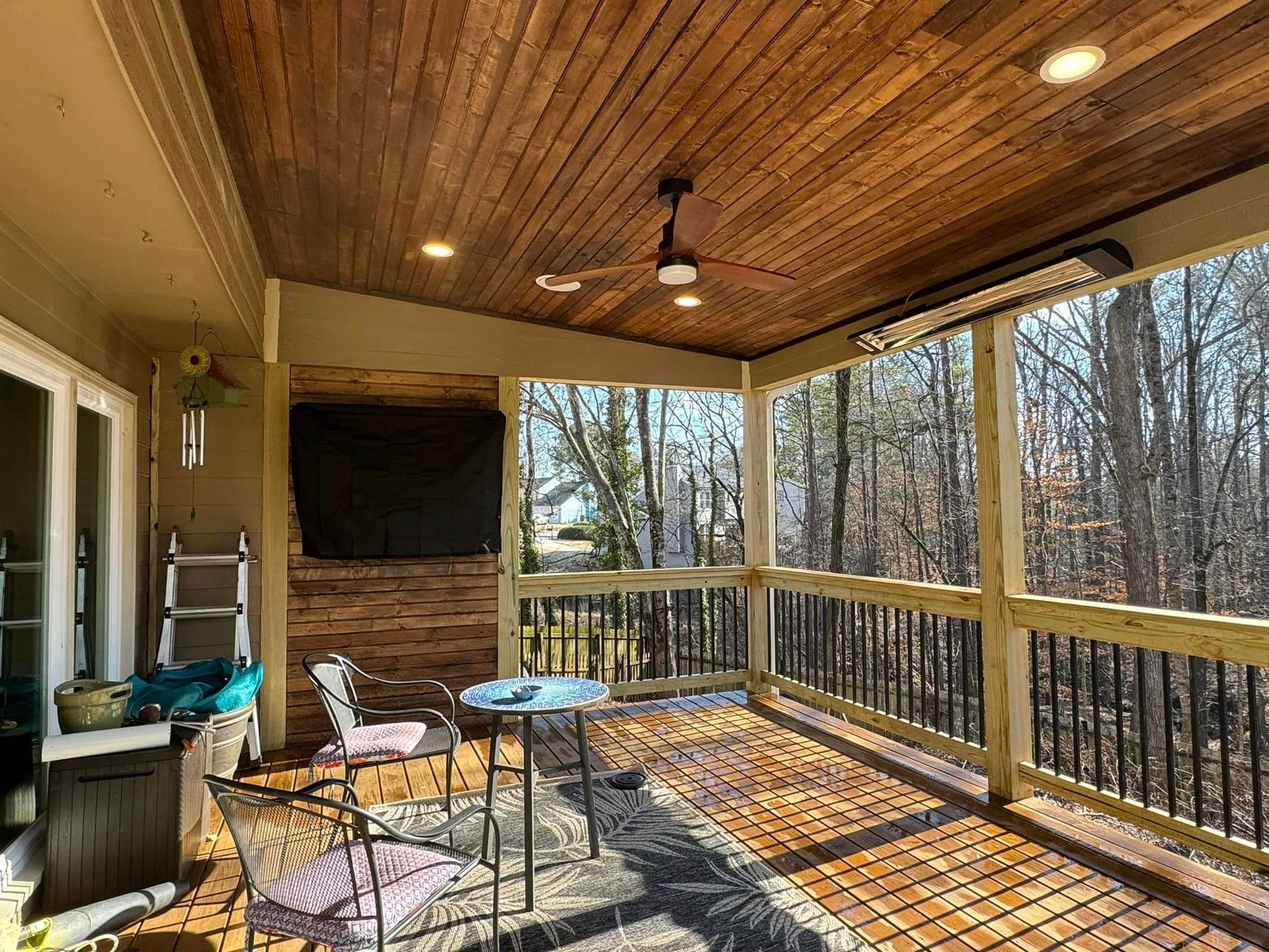 Outdoor covered patio with wood ceiling, dark metal railing, and a view of trees.