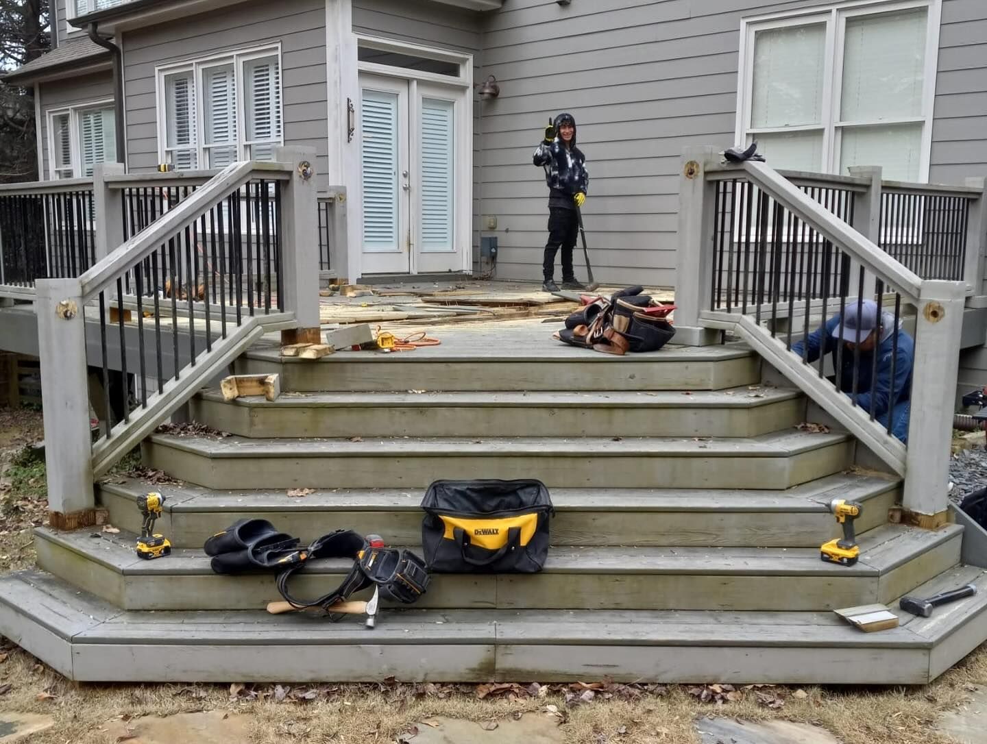 Workers rebuilding wooden deck stairs. Tools and materials are scattered around.