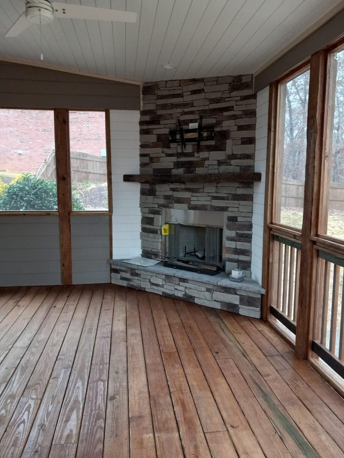 Sunroom interior with stone fireplace, wooden floor, and large windows.