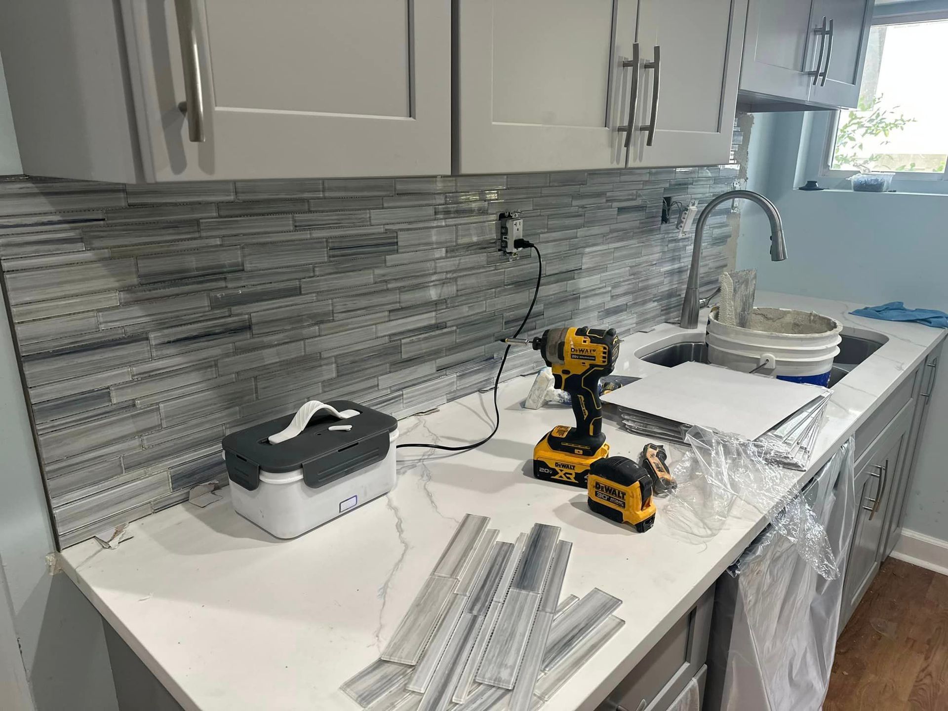 Kitchen backsplash under construction; tools and materials on the countertop.