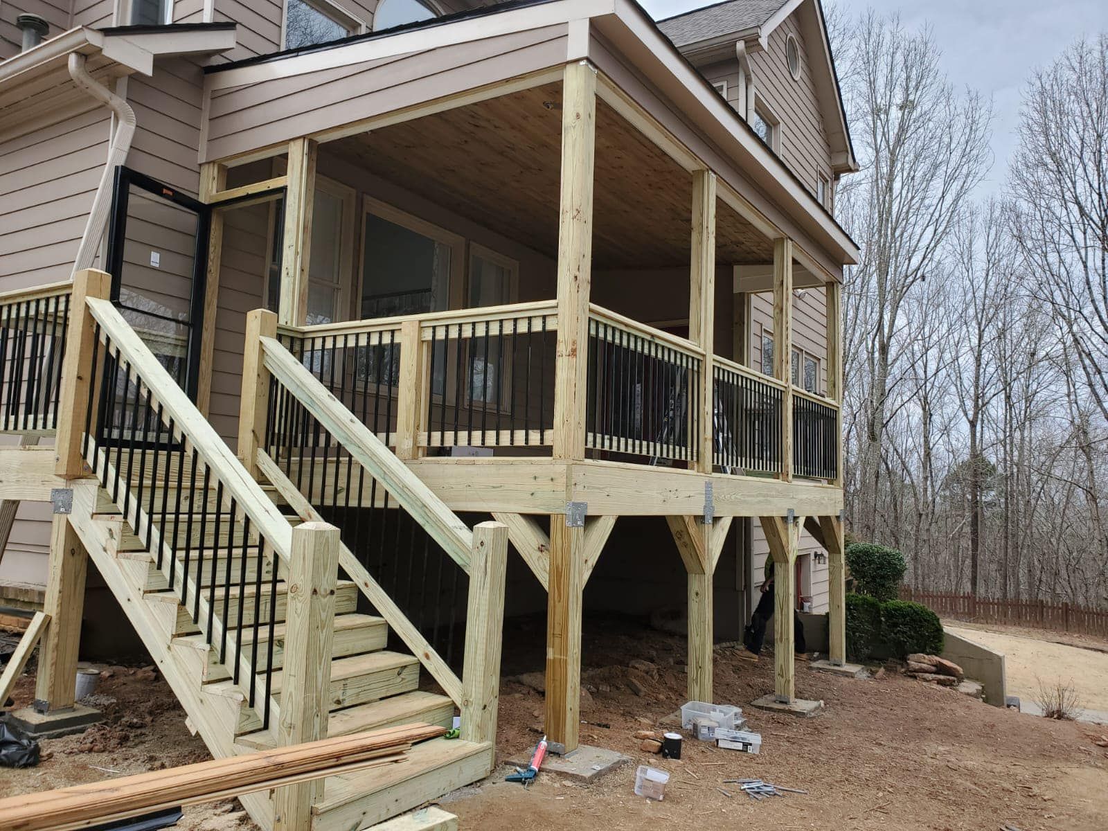 Wooden deck and stairs attached to a house with black railings and a covered porch.