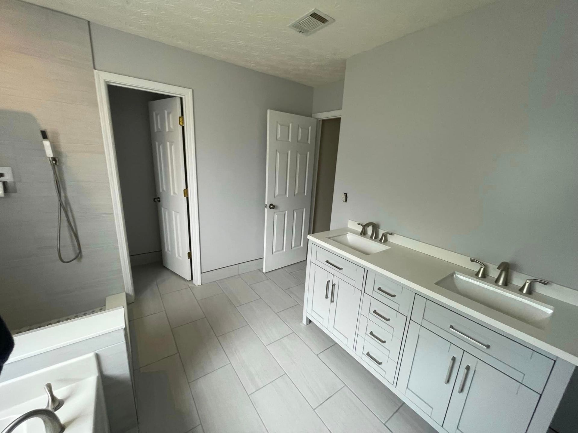 Bathroom with gray walls, white cabinets, and two sinks. Two doors visible, one open.