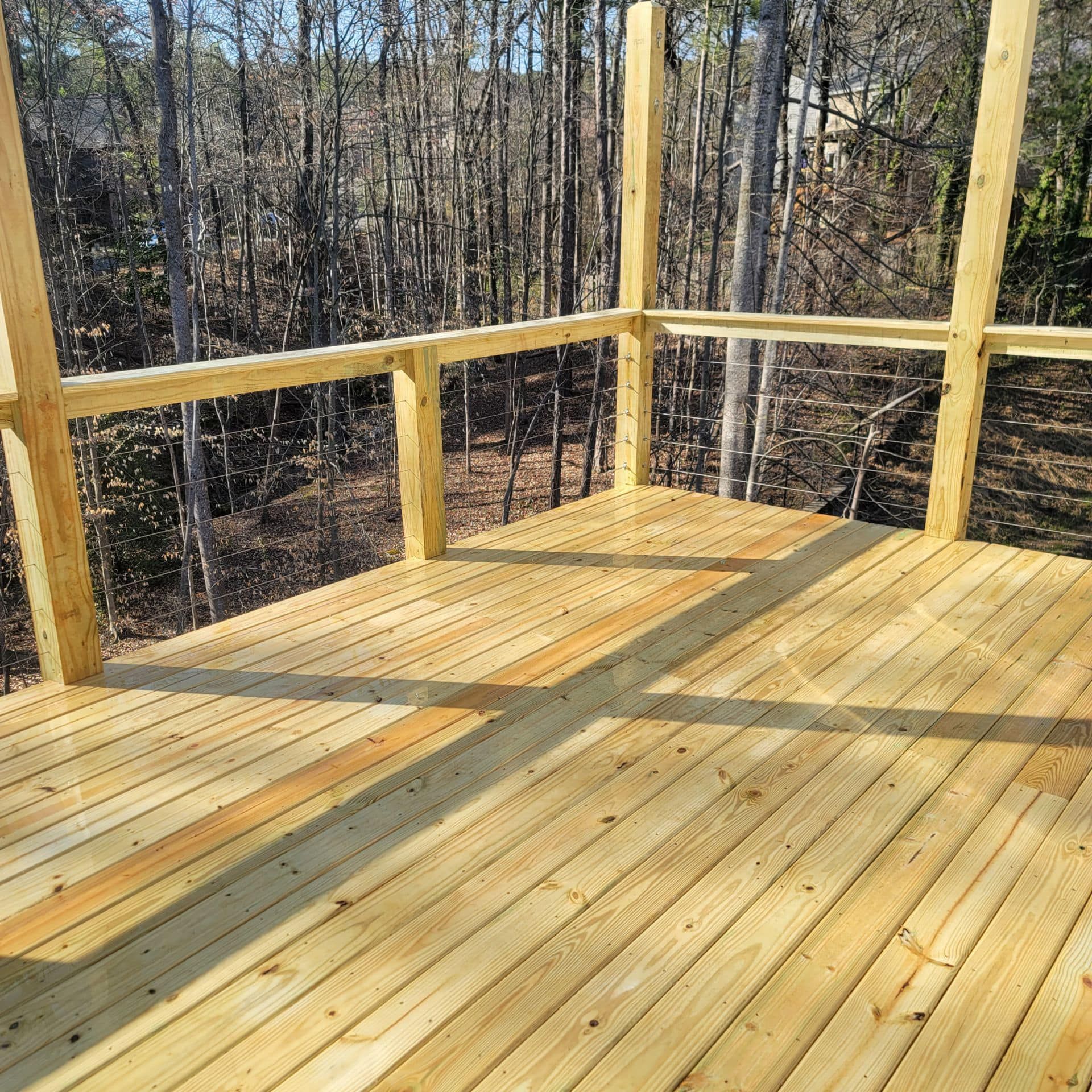 Newly built wooden deck with railing in a wooded setting.
