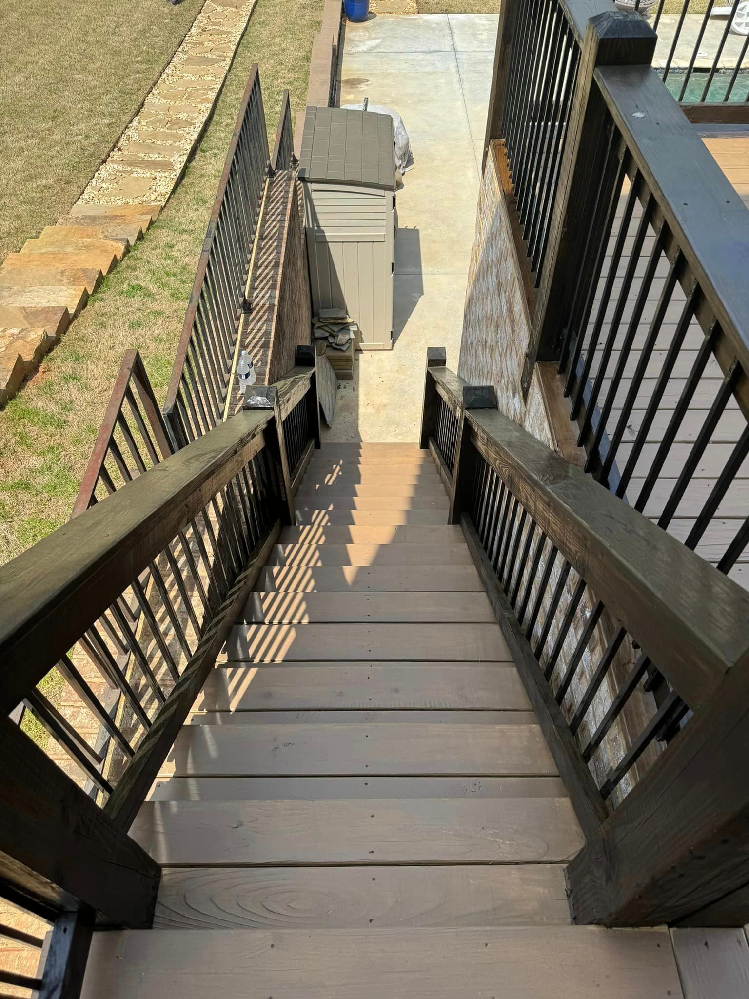 Wooden stairs leading down, flanked by railings. Sunlight casts shadows.