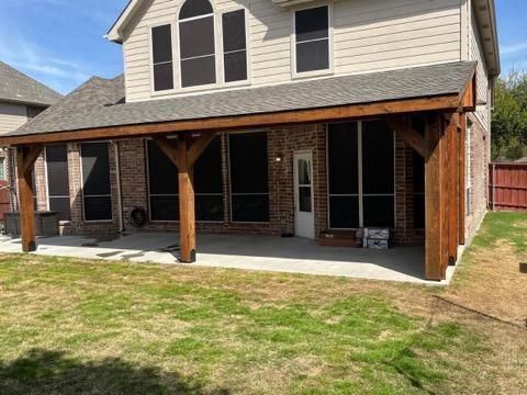A backyard patio with a wooden pergola attached to a brick home.