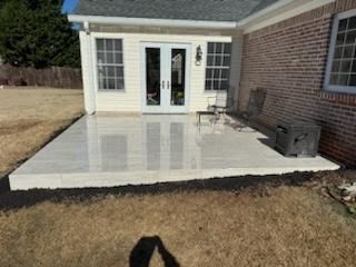 Concrete patio outside a house with a brick wall, doors, and windows, surrounded by grass.