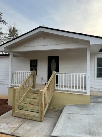 White house with porch and wooden steps, black door. Light beige foundation and gray concrete.