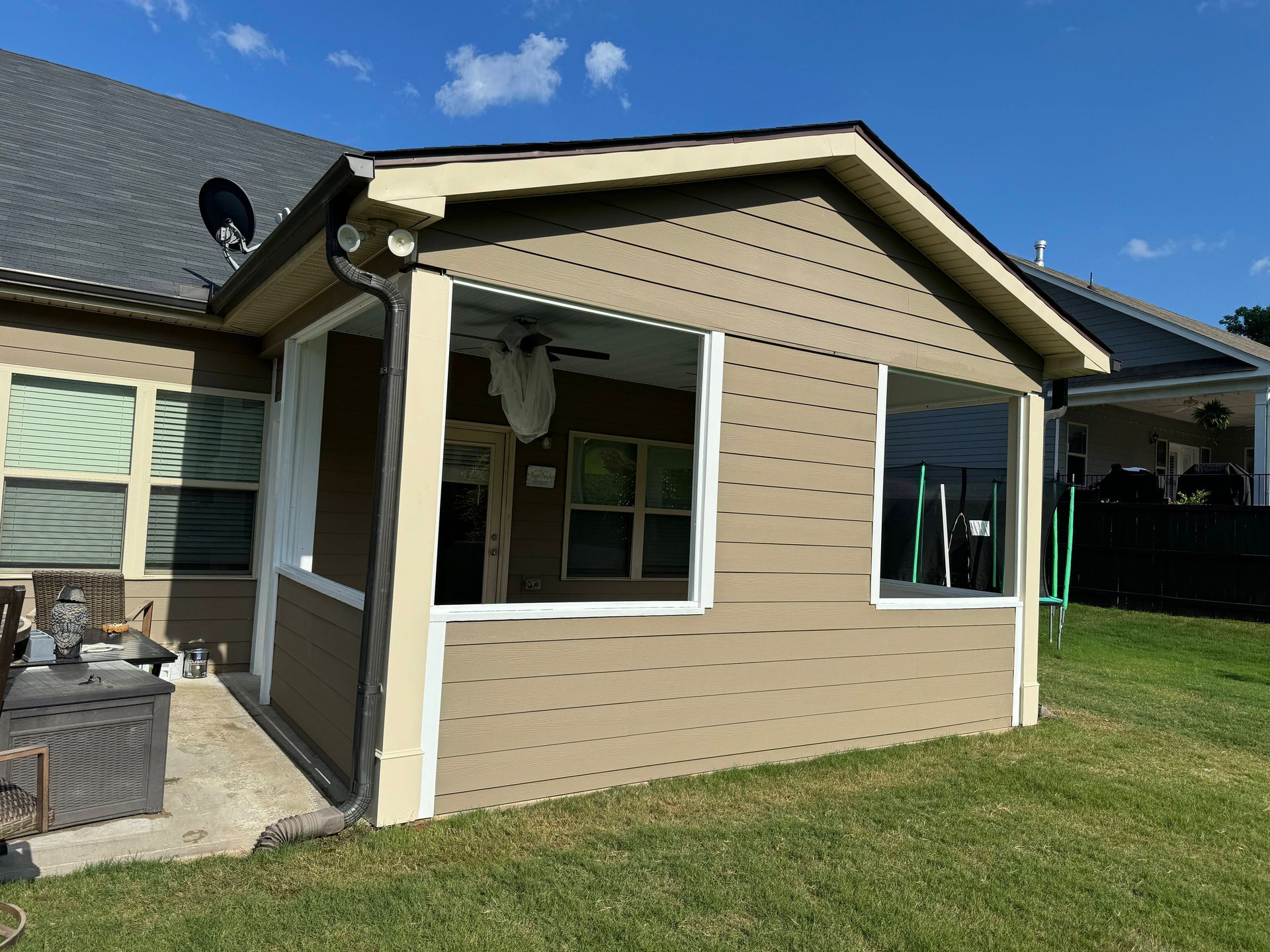 Tan screened-in patio attached to a house with white trim, set in a grassy yard.