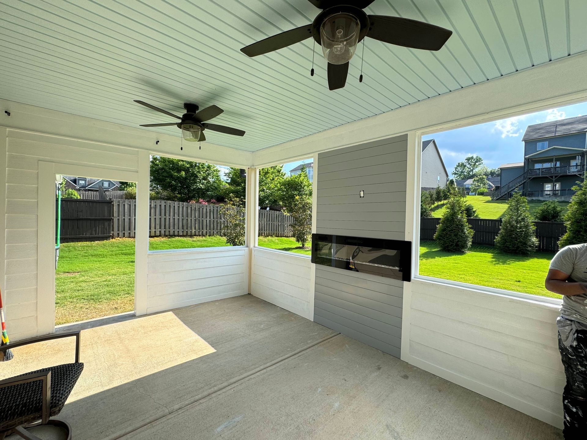 Screened porch with white walls, concrete floor, ceiling fans, and an outdoor fireplace.