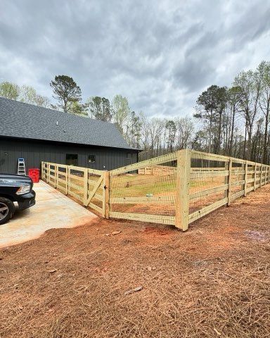 Wooden fence surrounding a yard, with a gate, next to a dark-colored building.