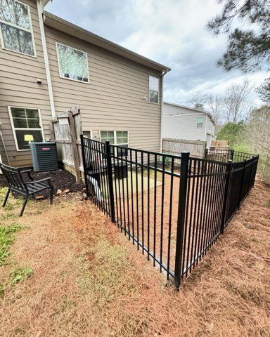 Black metal fence in a yard next to a beige house, under a cloudy sky.