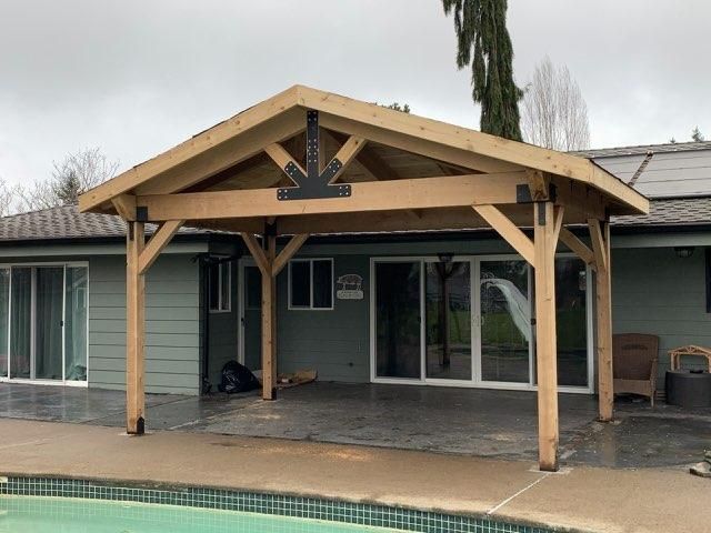 Wooden-framed patio cover over a concrete patio near a pool, attached to a house with sliding glass doors.