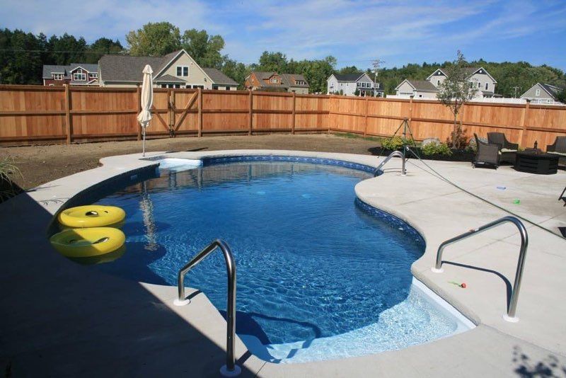 Backyard pool with blue water surrounded by concrete, wooden fence, and yellow floats.