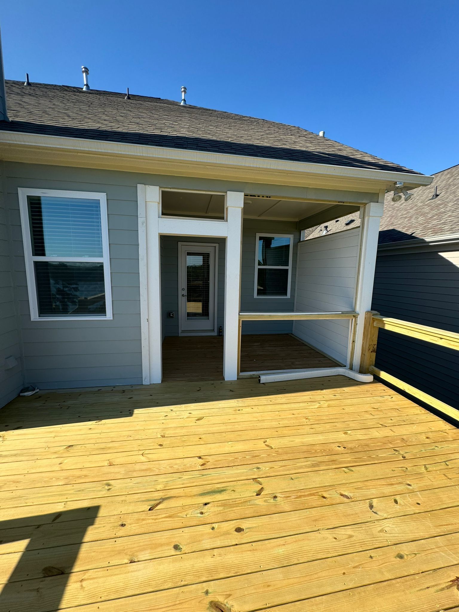 Exterior of a house under construction; wooden deck, covered porch, light blue siding, and clear sky.