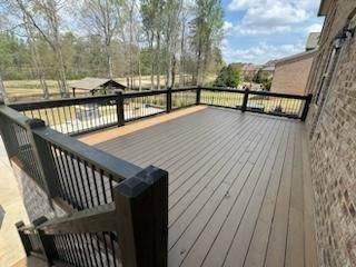Elevated wooden deck with dark railing and stairs, attached to a brick house, overlooking a grassy area.
