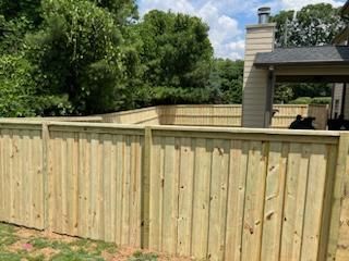 Wooden fence surrounding a backyard with trees and a house.