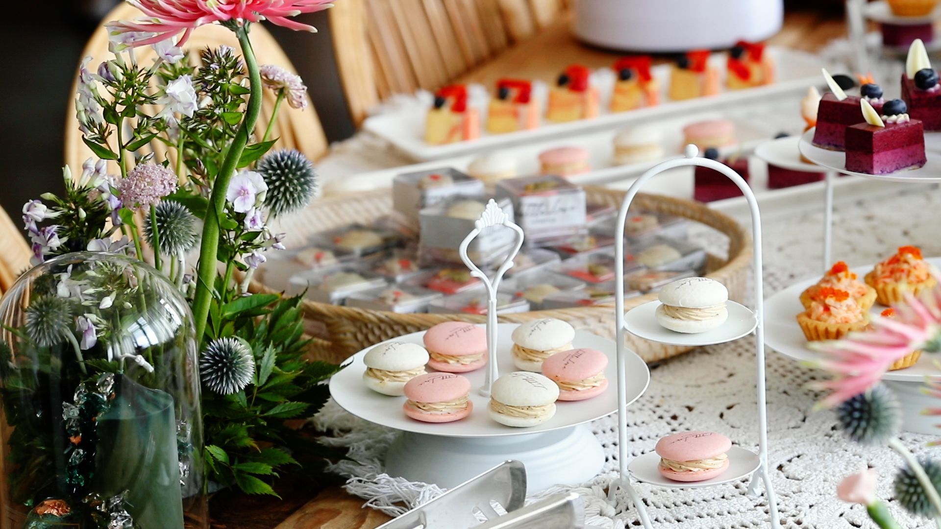Dessert table with macaroons, cakes, and flowers; white and pink color scheme.
