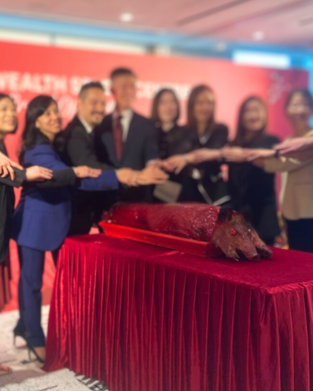 People reaching toward a roasted pig on a red table, likely for a celebration or event.