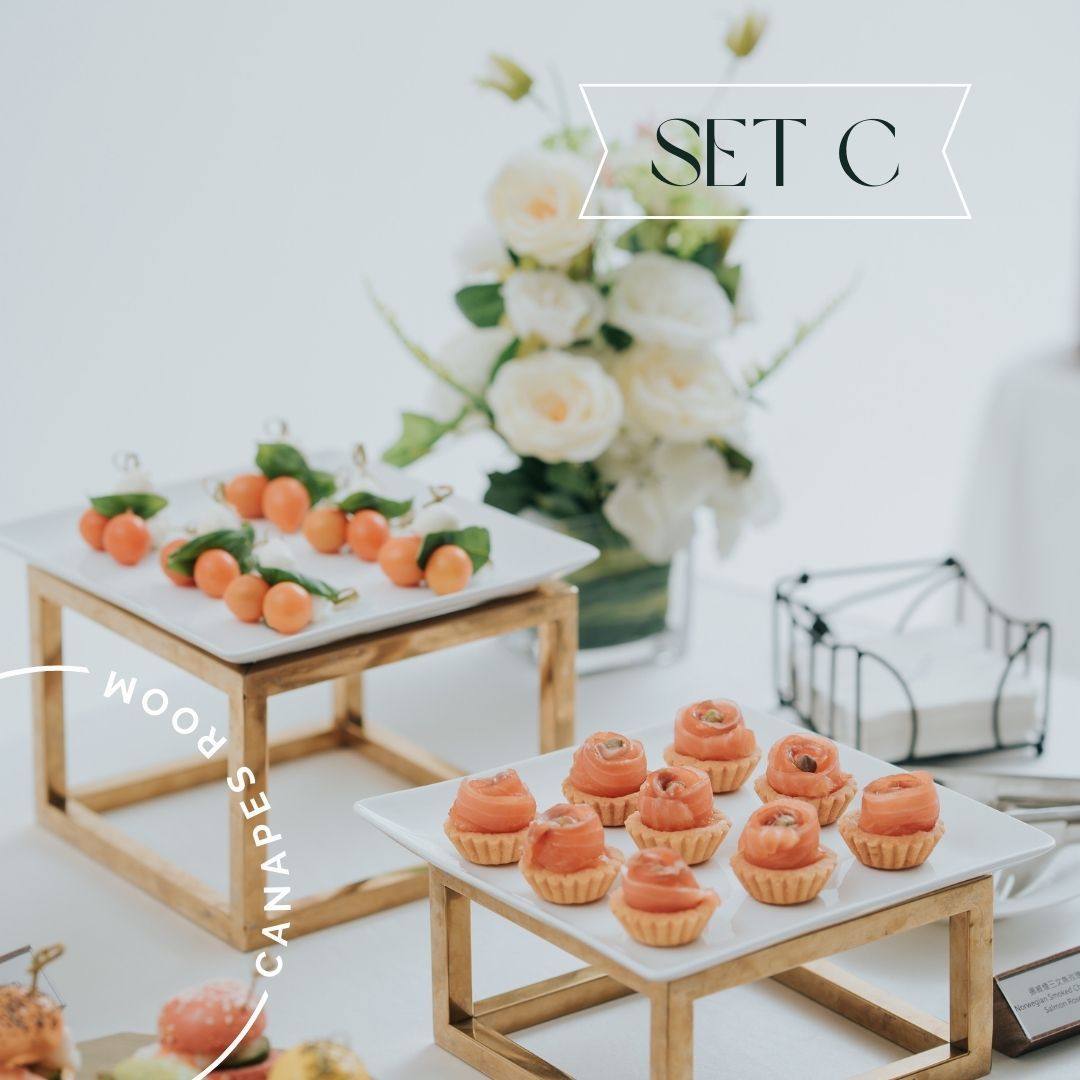 Canapés on white rectangular trays, on wood and gold stands, next to flowers and napkins.