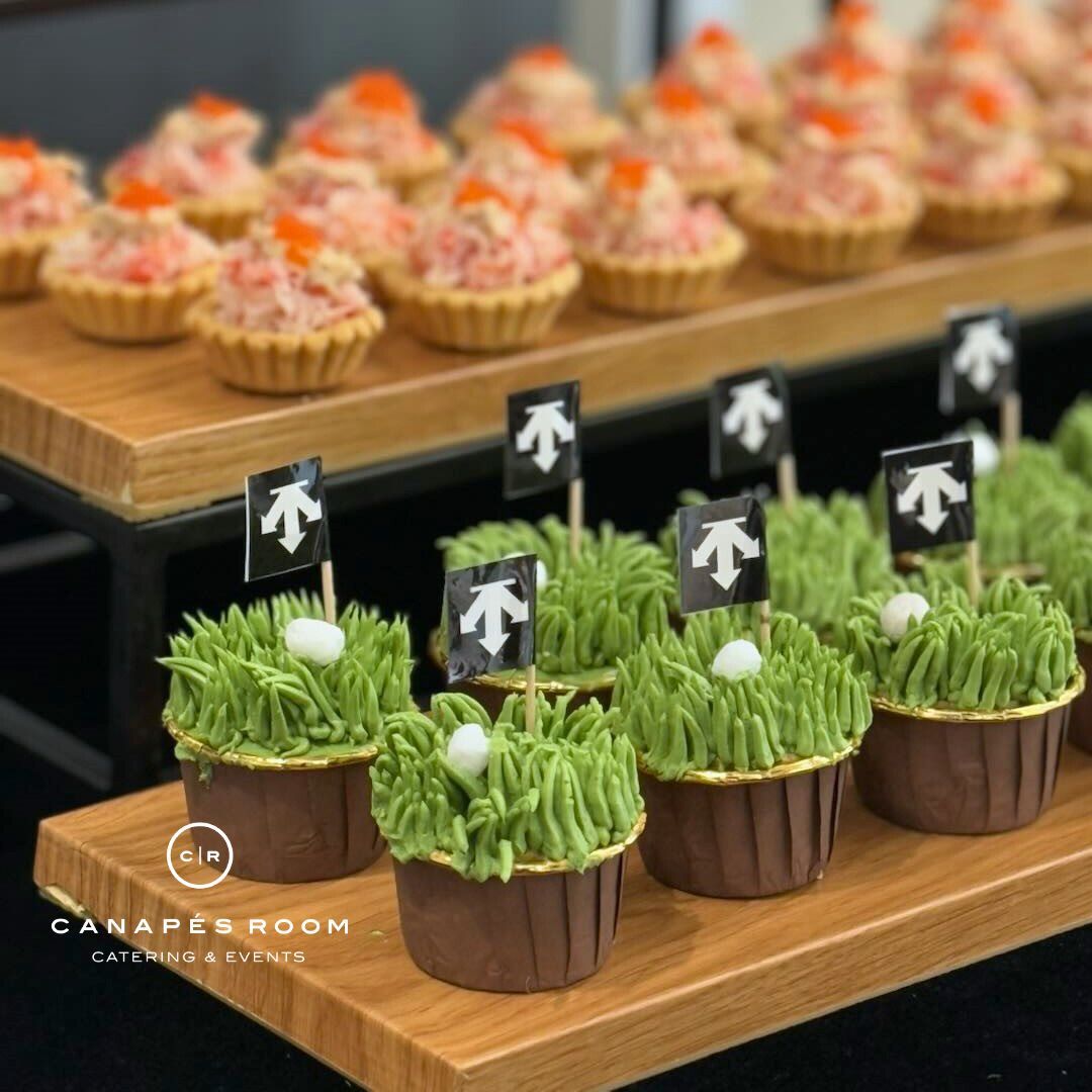 Mini crab salad tarts and golf-themed cupcakes with edible grass and flags on wooden platters.