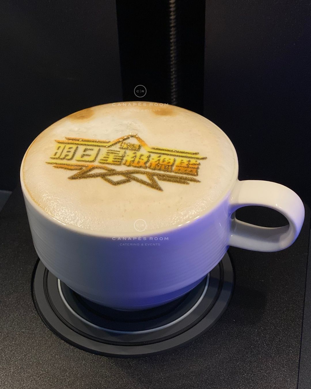 Latte in a white cup, with logo printed on foam, on a black coffee machine base.