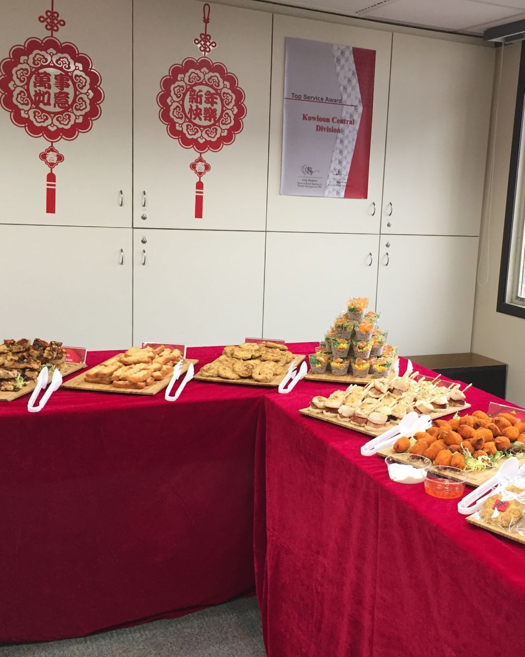 Buffet table with various snacks, red tablecloth, Chinese decorations, white cabinets.