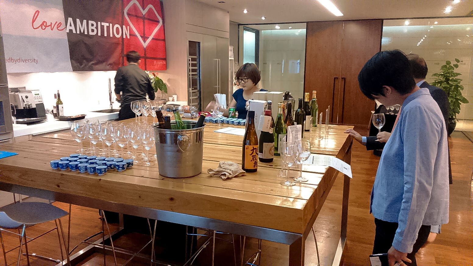 People at a bar, some looking at bottles. A banner reads