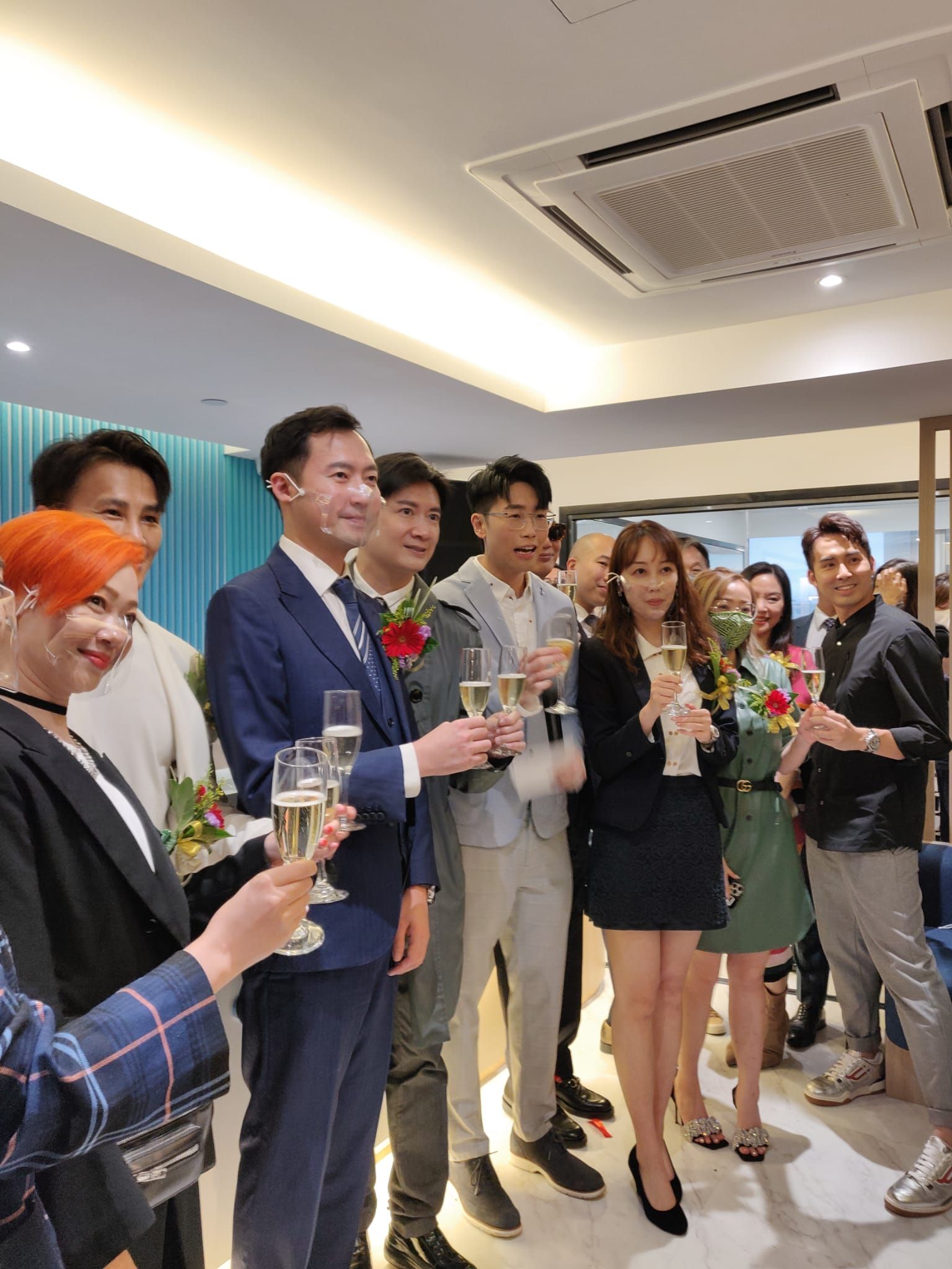 Group of people toasting with champagne flutes at an indoor event, likely a celebration or opening.