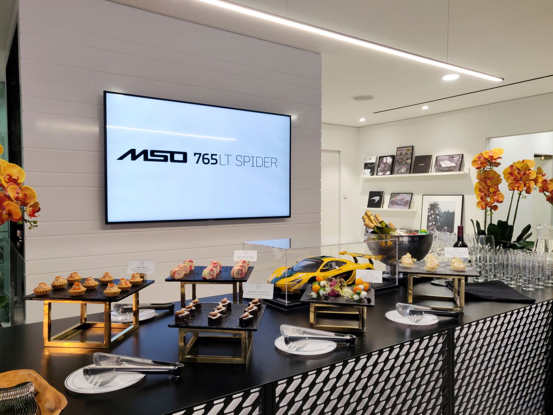 Buffet table at an event, with appetizers and a model car under a screen displaying